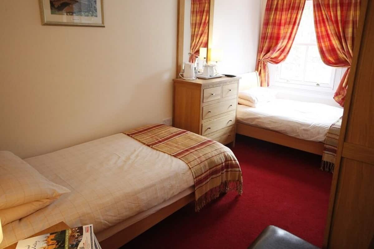 A bedroom with two single beds, a wooden dresser, a mirror, and a window with curtains.