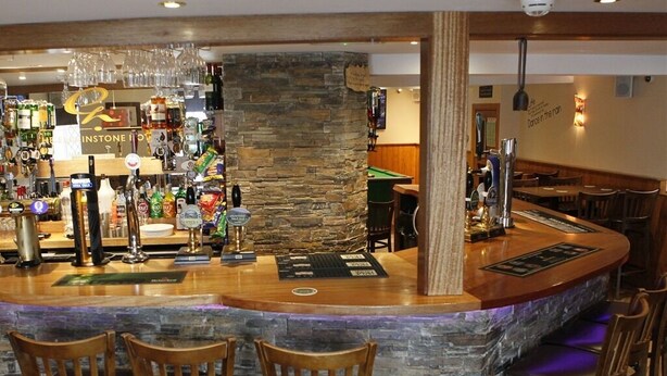 Eine Bar mit einer Steintheke, mehreren Zapfhähnen und Barhocker.