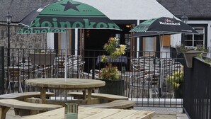Ein Sitzbereich im Freien mit Holztischen und -stühlen sowie zwei Heineken-Schirmen.