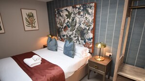 Ein ordentlich bezogenes Bett mit roter Decke, ein Nachttisch mit Lampe und ein Wandteppich mit Blumenmuster.