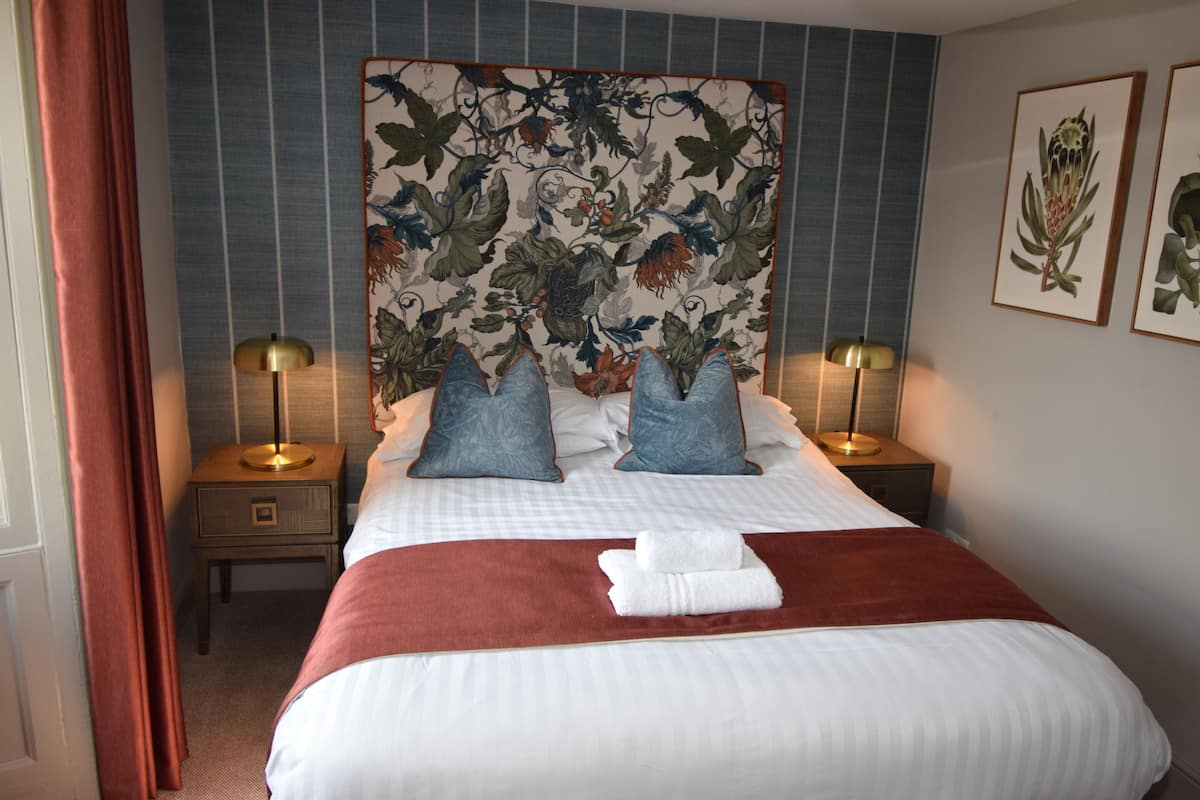A neatly made bed with a floral headboard, two bedside tables with lamps, and a red accent on the bed.