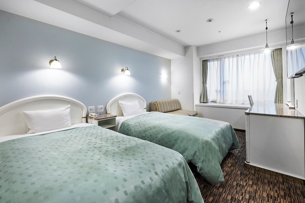 Habitación de hotel con dos camas, un escritorio, una ventana con cortinas e iluminación empotrada.