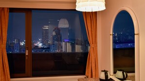 A room with a large window offering a nighttime city view, a white lamp, and a small table with a kettle. - Kobe Sannomiya Union Hotel (Kobe)