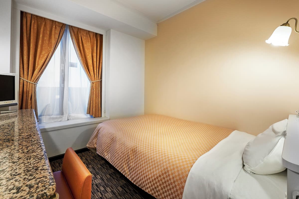 Habitación de hotel con cama, escritorio, silla y ventana con cortinas.
