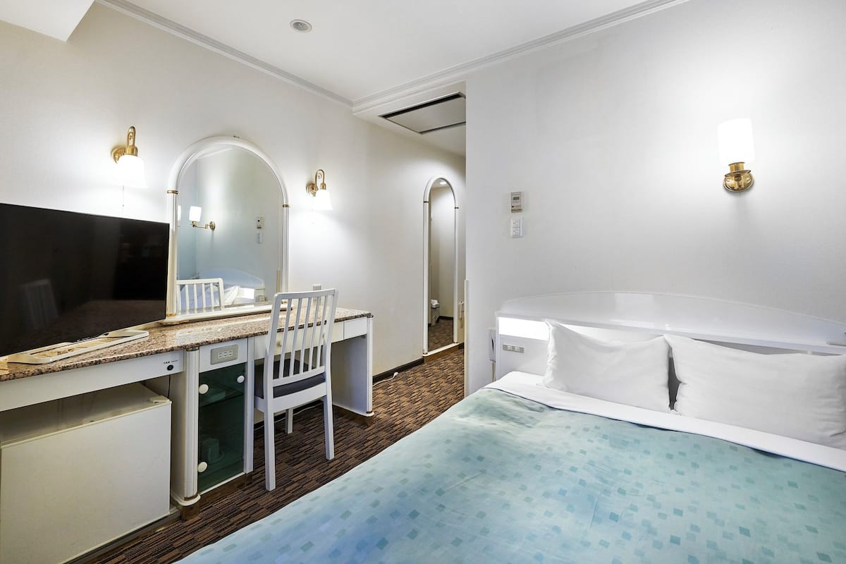 Habitación de hotel con cama, escritorio con silla, espejo grande y dos luces fijadas a la pared.