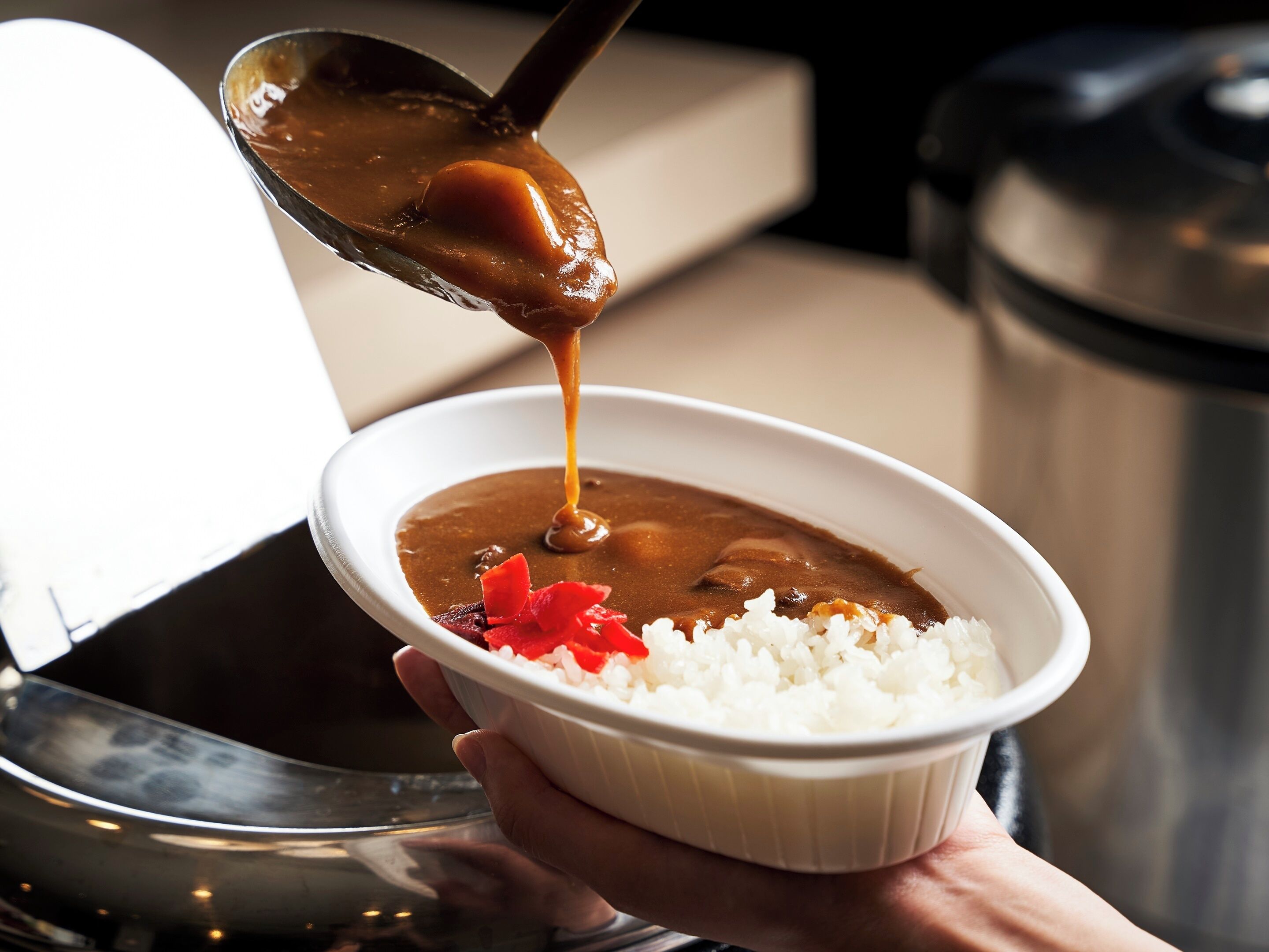 A person holding a bowl of rice and curry, with a spoon lifting some curry.