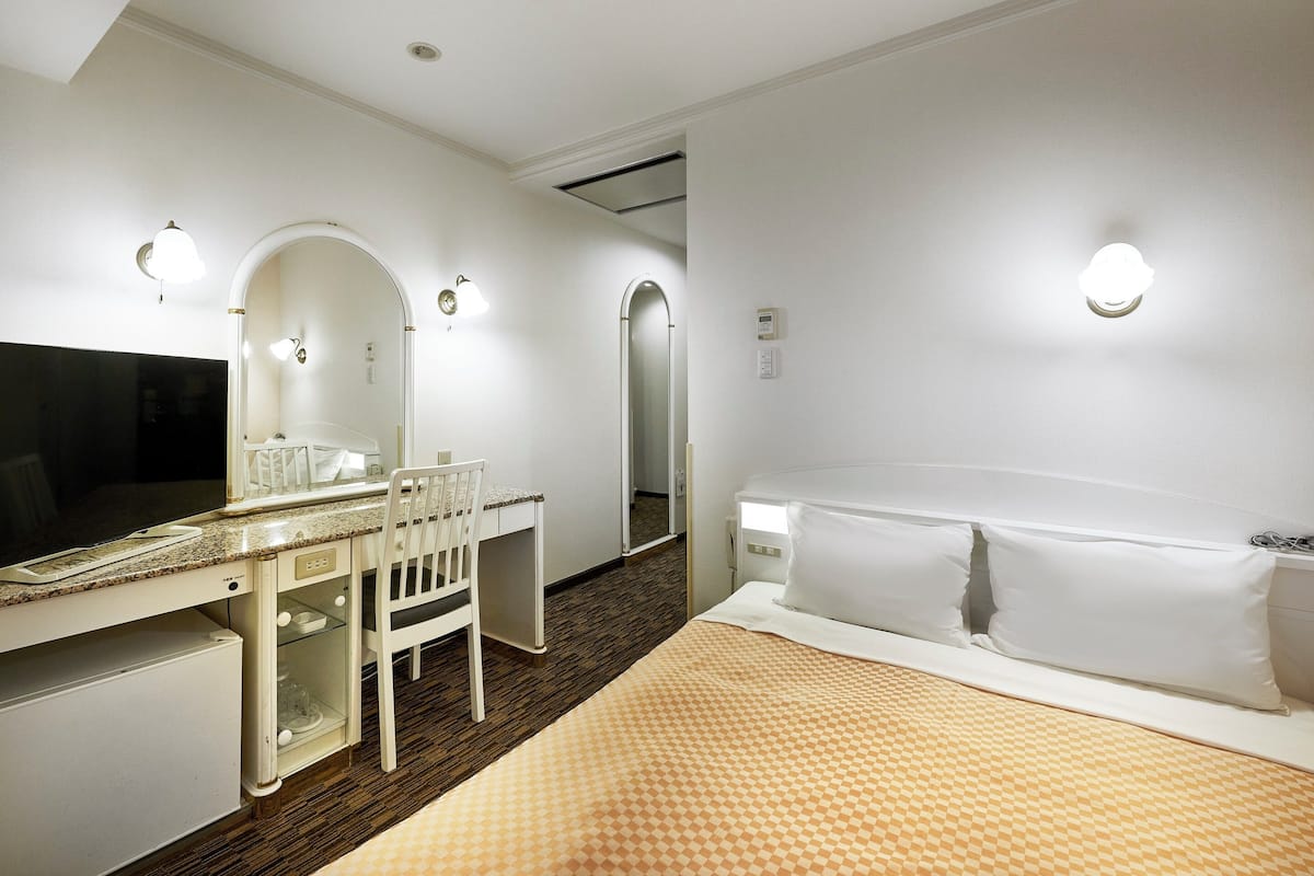 Una habitación de hotel con cama, escritorio, silla, espejo y tocador.