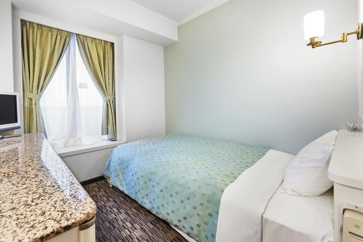 Habitación de hotel con cama, escritorio con computadora, ventana con cortinas y lámpara de pared.
