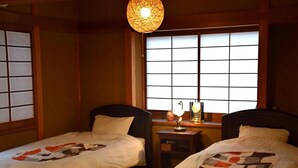 A traditional Japanese-style room with two beds, a small desk, and a shoji screen window. - Guest House Higashiyama (Kyoto)