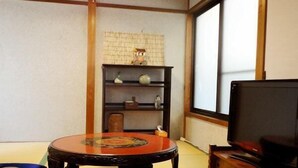 A tatami mat room with a low table, a television on a wooden stand, and a shelf with decorative items. - Guest House Higashiyama (Kyoto)
