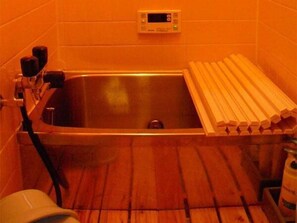 A bathroom with a stainless steel sink, a digital thermostat, and wooden planks on the floor.