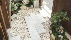 A pathway with stepping stones, pebbles, and small plants leading to a wooden door. - Guest House Higashiyama (Kyoto)