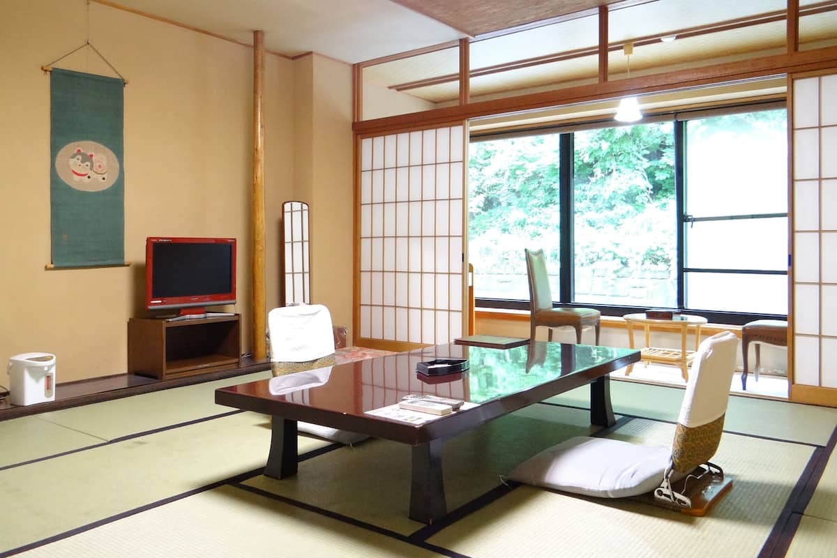 Una habitación japonesa tradicional con suelo de tatami, una mesa baja, dos esteras de tatami, un televisor y un biombó shoji.