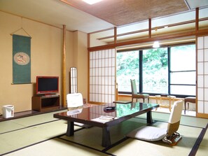 Een traditionele Japanse kamer met tatami vloeren, een lage tafel, twee tatami matten, een televisie en een shoji scherm.