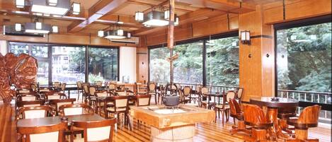 A spacious indoor area with wooden flooring, multiple tables and chairs, and large windows offering views of the outdoors.