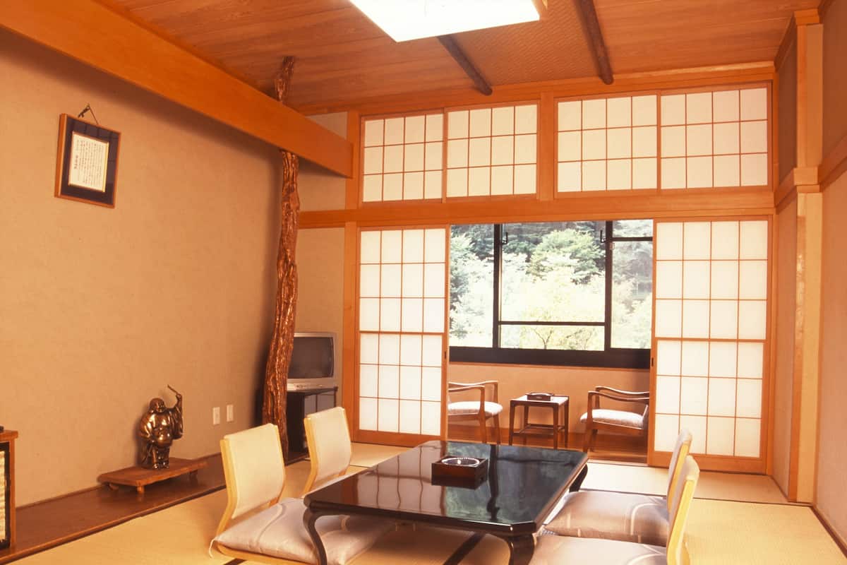 Una habitación japonesa tradicional con suelo de tatami, una mesa baja con cojines y puertas correderas shoji.