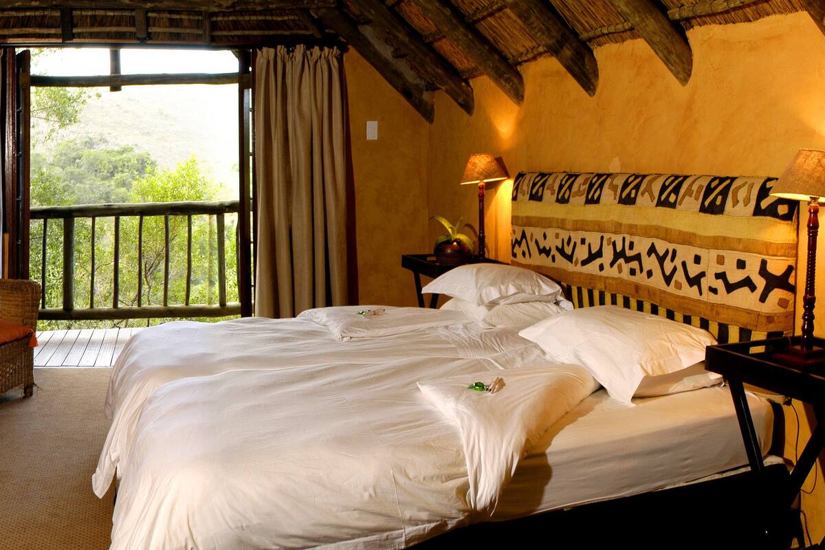 A bedroom with a large bed, a chair, a small table with a lamp, and a window with curtains.