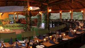 An outdoor dining area with tables set for a meal, surrounded by chairs and a fire pit. - Lalibela Game Reserve (Grahamstown)