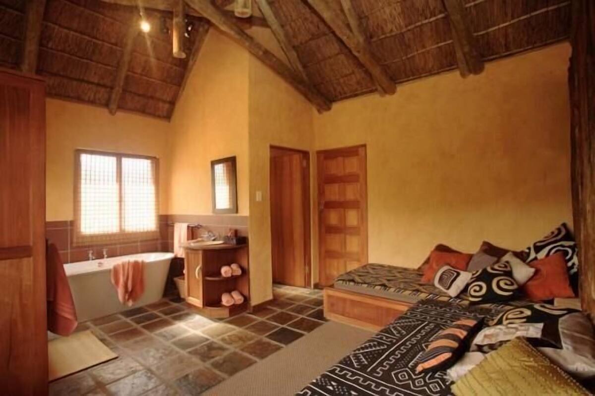 A room with a bathtub, a wooden wardrobe, a bed with patterned pillows, and a window with a view.