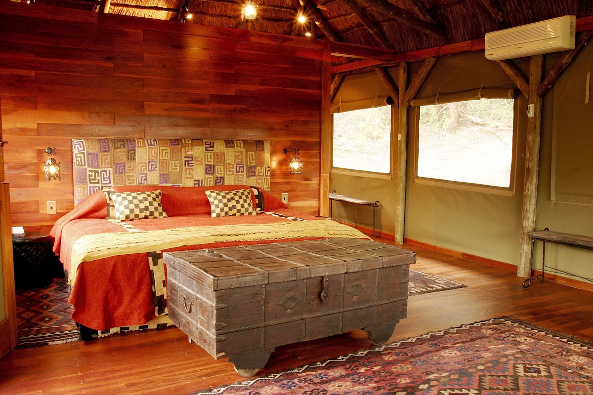 A wooden-themed bedroom with a bed, a chest of drawers, and a window.