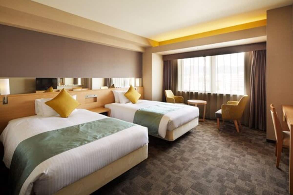 A hotel room with two beds, a small table, a chair, and a TV.