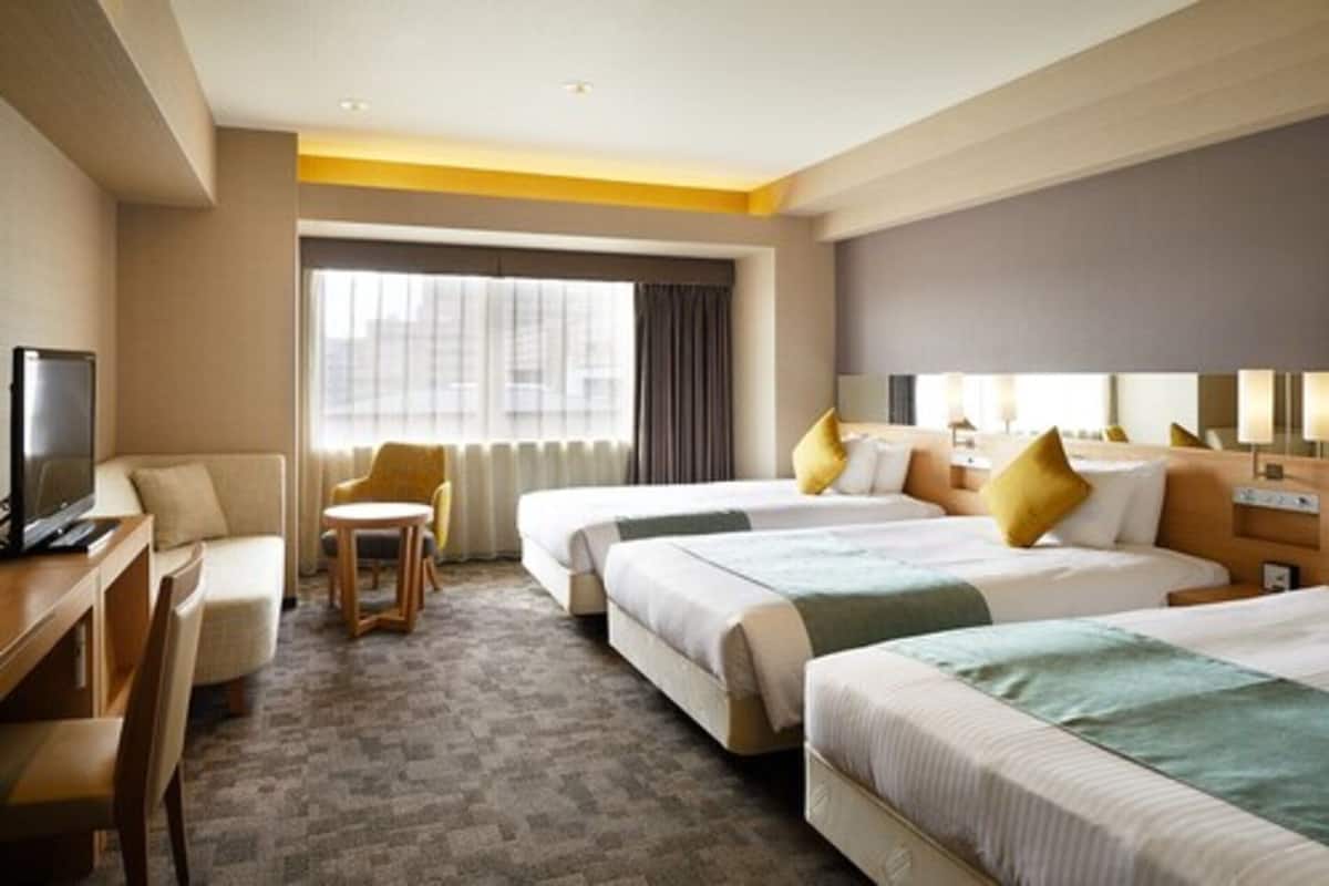 A hotel room with two beds, a desk, a chair, a TV, and a large window with curtains.