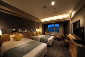 A hotel room with two beds, a desk, a TV, and a window with a view.