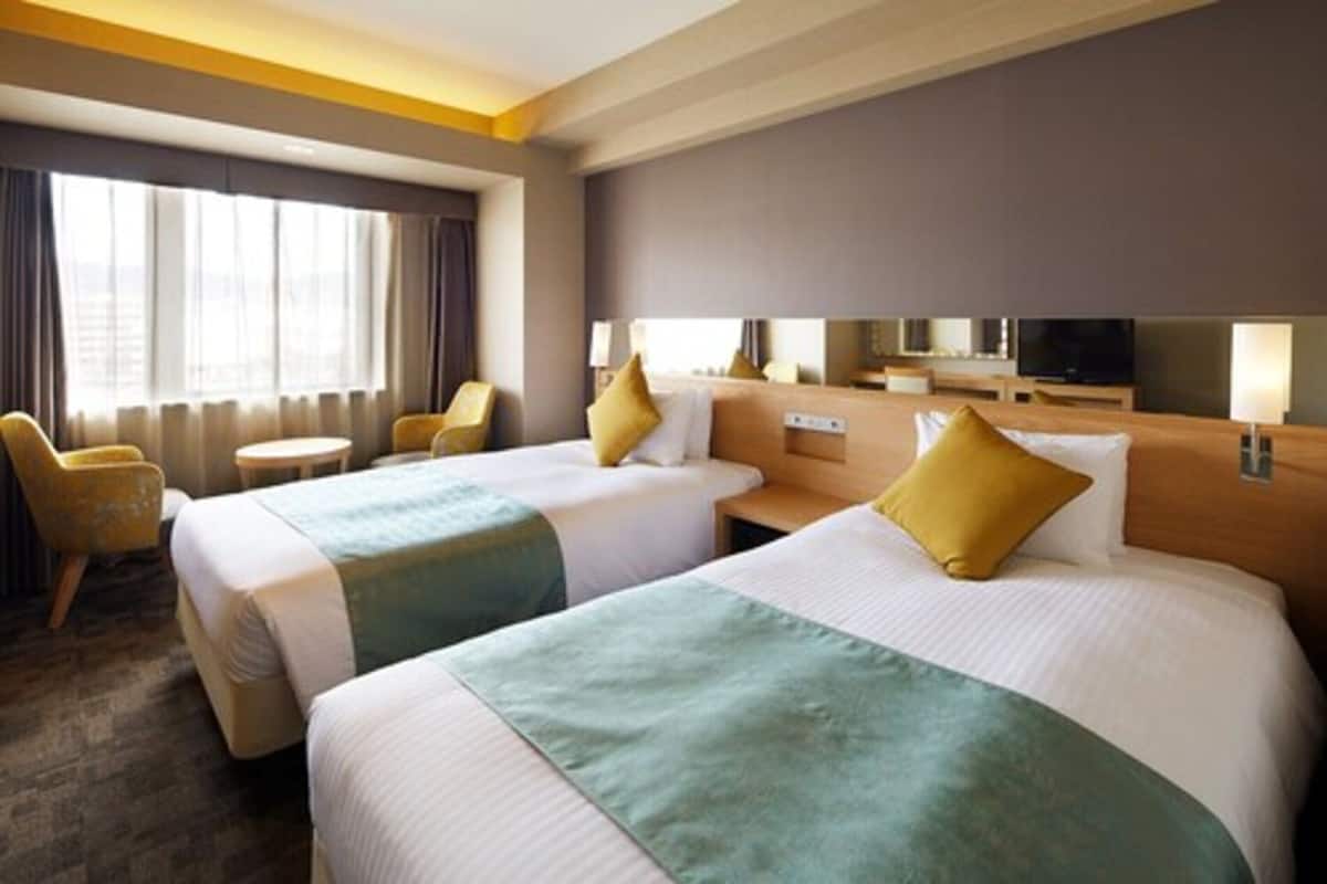 A hotel room with two beds, a TV, a desk, and a chair.