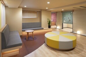A modern waiting area with a sofa, a small round table, and a colorful ottoman. - Almont Hotel Kyoto (Kyoto)