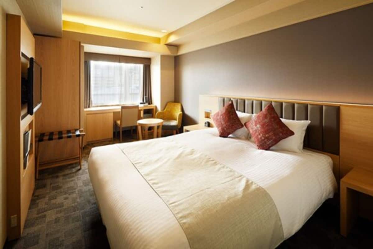 A hotel room with a large bed, a television, a desk, and a chair.