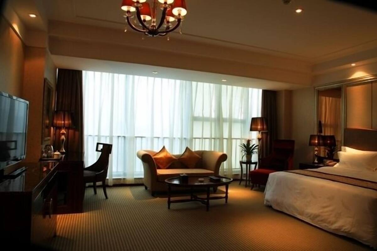 Una habitación de hotel con cama, sofá, mesa de centro, escritorio y televisor.