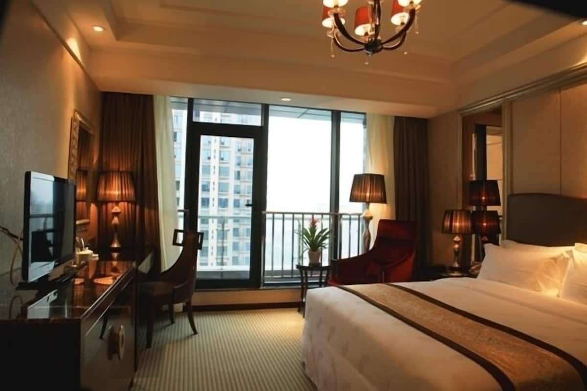 Habitación de hotel con una cama grande, un escritorio con silla, televisión y balcón con vistas a la ciudad.