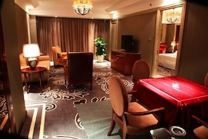 Una habitación de hotel con una mesa de comedor, sillas, televisor, cama y una planta.