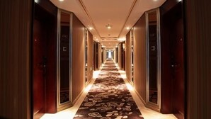 Un largo y estrecho pasillo de hotel con puertas de madera a ambos lados y una alfombra estampada.