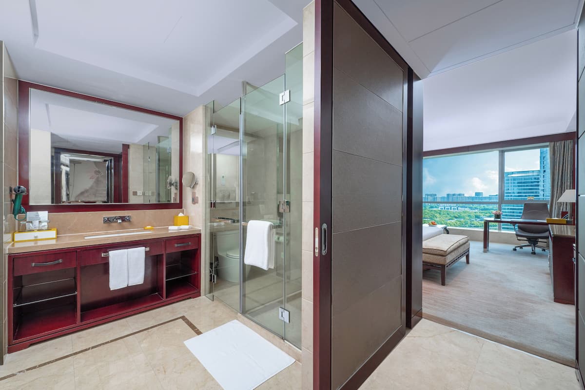 A modern hotel bathroom with a glass-enclosed shower, a large mirror, and a vanity with a towel rack.