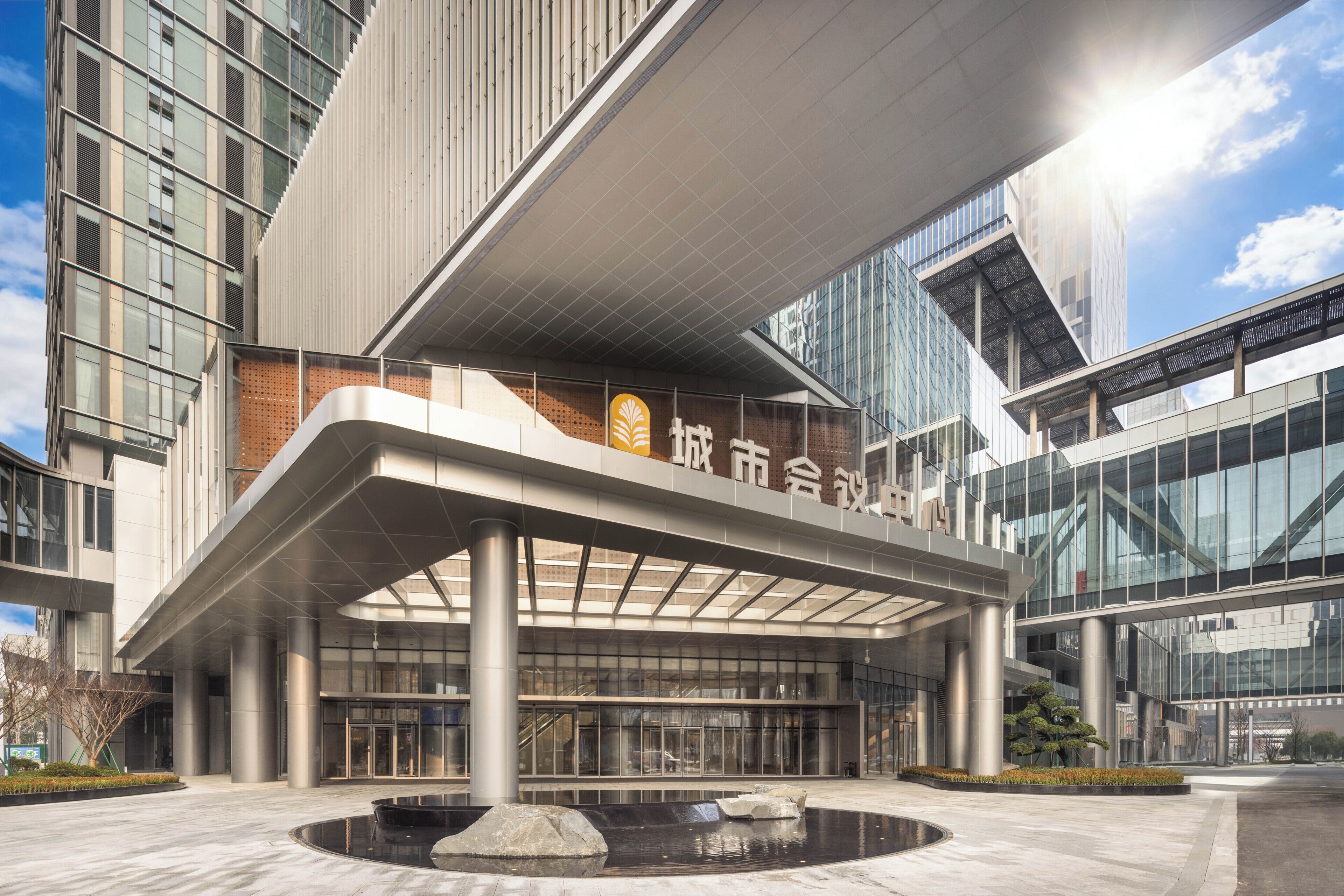 Un edificio moderno con una entrada destacada, grandes ventanales y una fuente central.