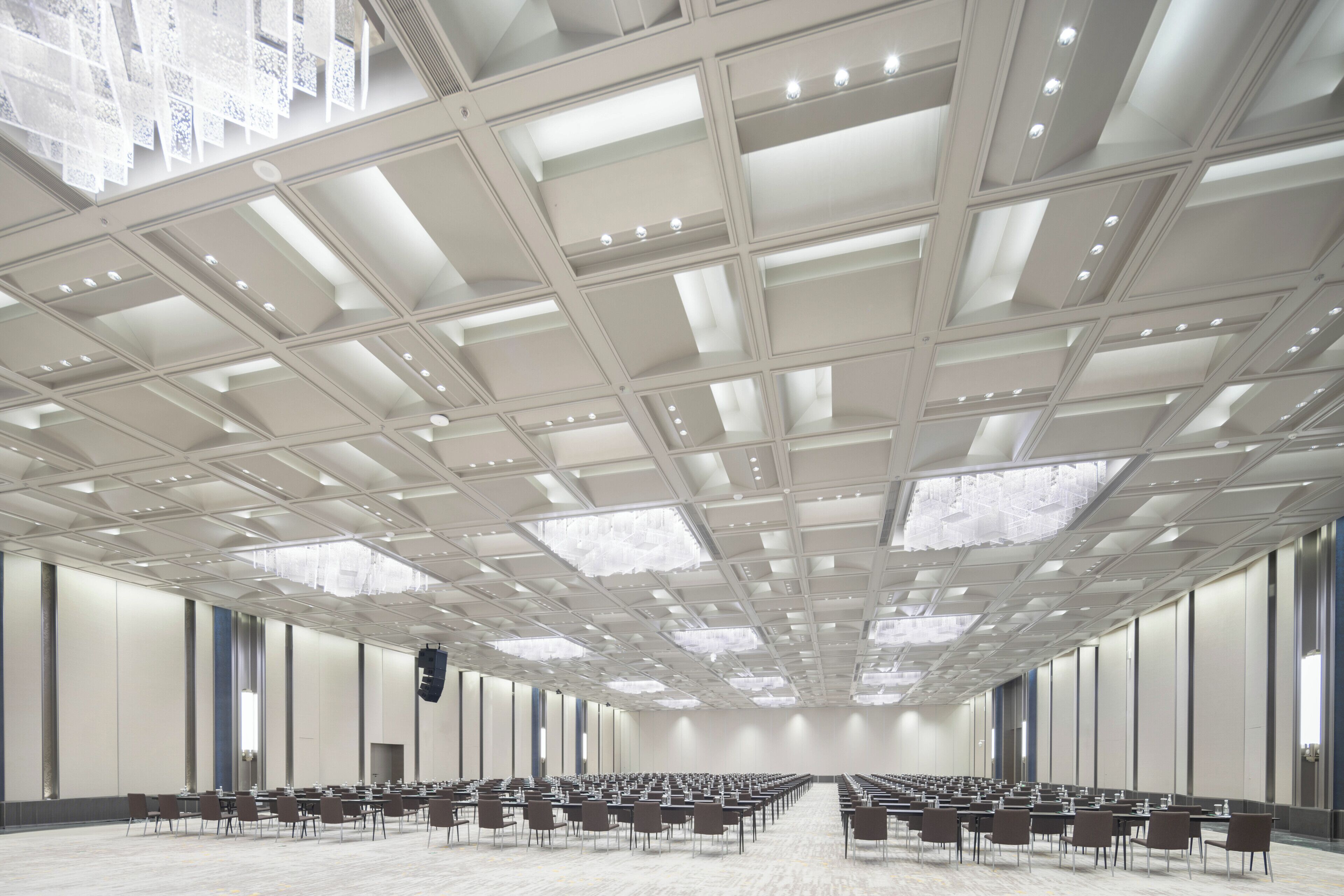 Une salle de conférence spacieuse, dotée d’un haut plafond, de rangées de tables et de chaises, et de grandes fenêtres.