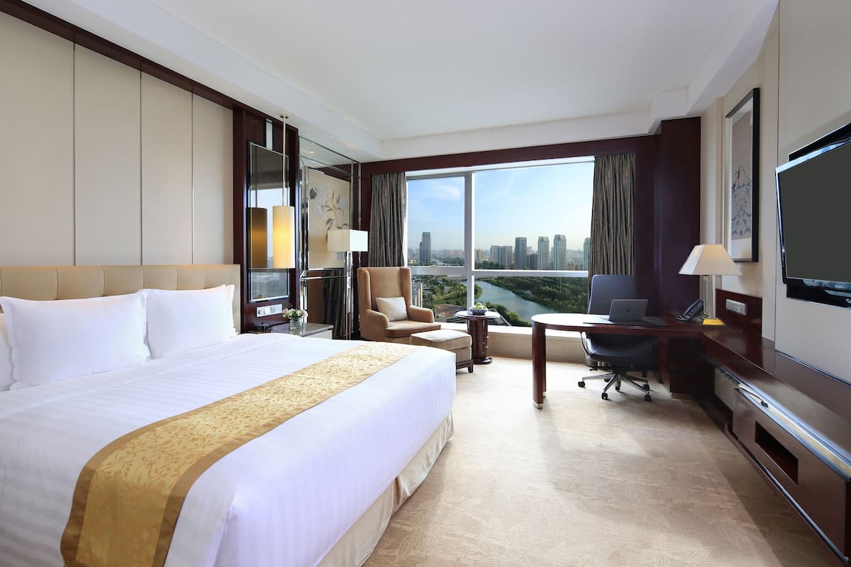 A hotel room with a large bed, a desk with a laptop, a chair, and a TV.