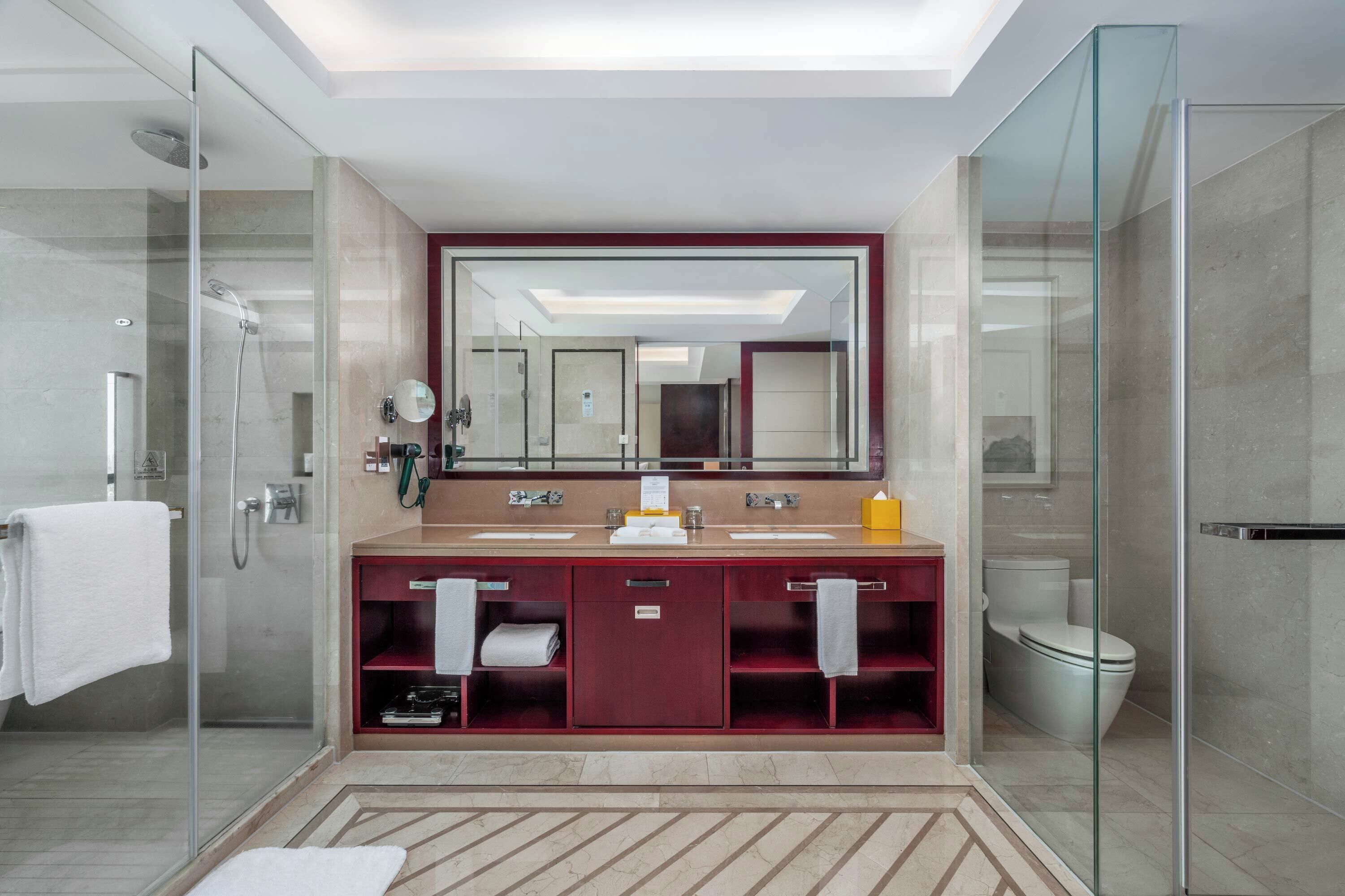 Un baño moderno con ducha de vidrio, un espejo grande y un tocador doble con un gabinete rojo.