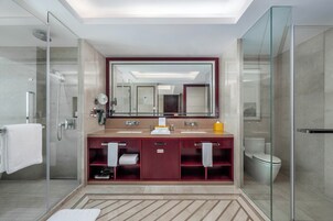 Un baño moderno con ducha de vidrio, un espejo grande y un tocador doble con un gabinete rojo.