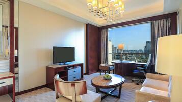 Ein Hotelzimmer mit Fernseher, einem Esstisch mit Stühlen, einer Couch und einem großen Fenster mit Blick auf die Stadt.