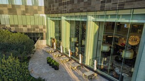 A modern building with a glass facade, outdoor seating area with tables and chairs, and a well-maintained garden. - Pan Pacific Ningbo (Ningbo)