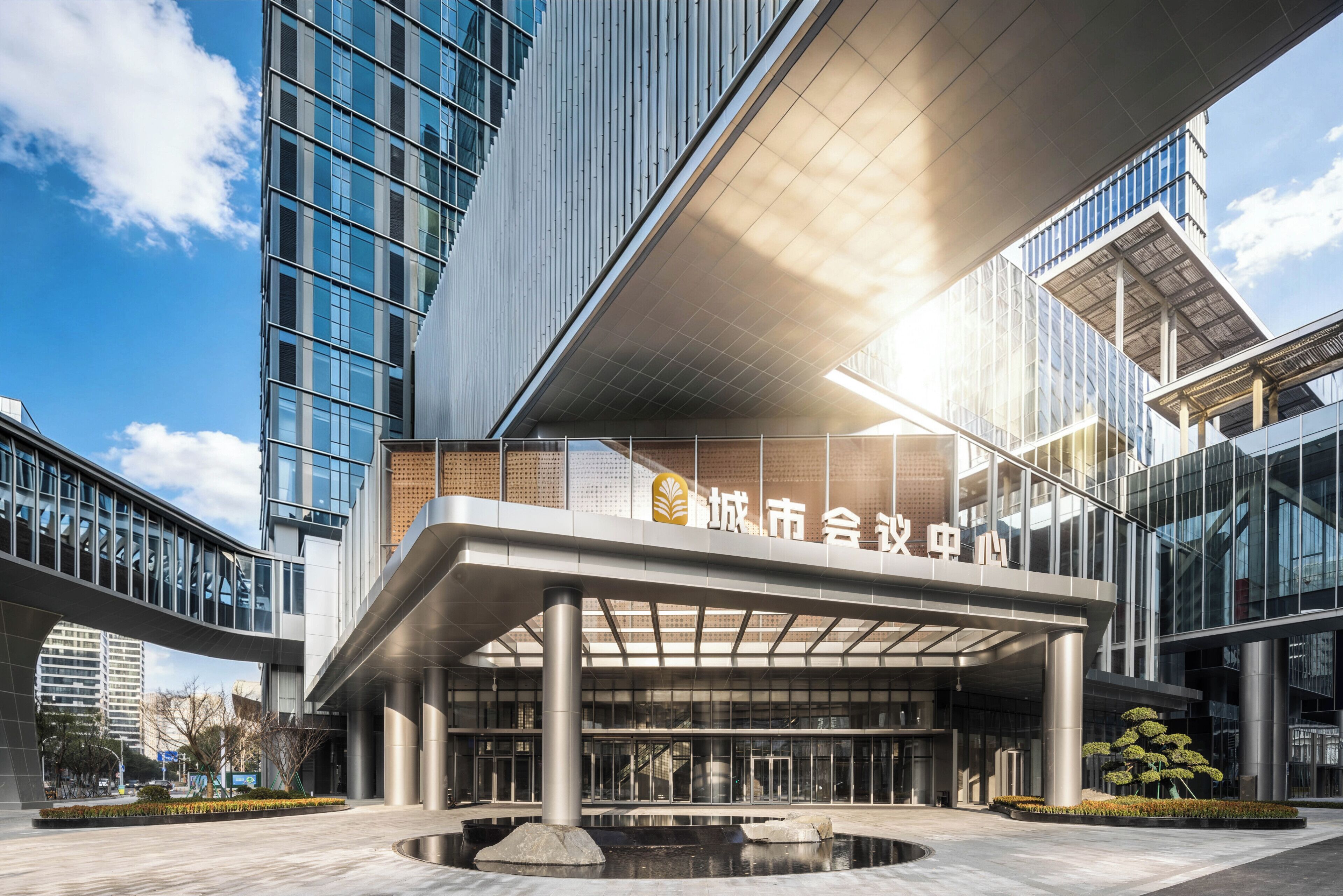 A modern building with a glass facade, a covered entrance, and a landscaped area with a water feature.