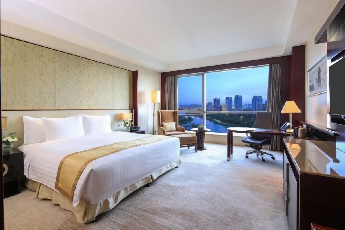 A hotel room with a large bed, a desk, a chair, and a TV.