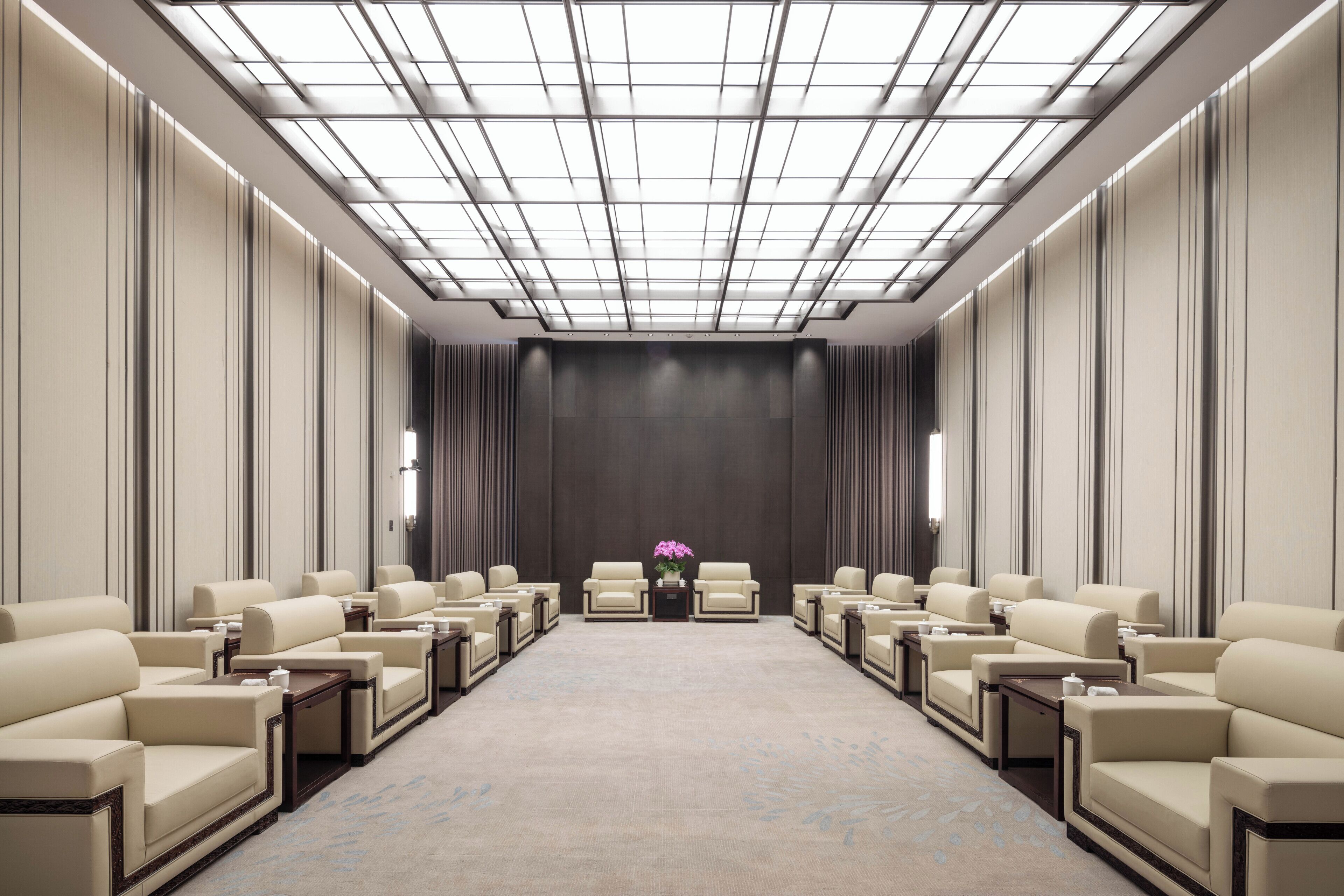 A conference room with a high ceiling, a central floral arrangement, and rows of leather chairs.