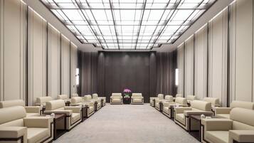 A conference room with a high ceiling, a central floral arrangement, and rows of leather chairs.