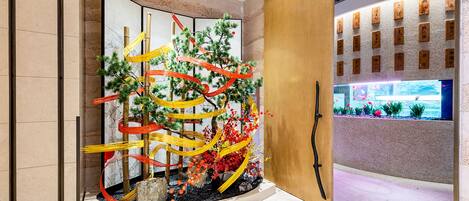 Zona de recepción con diseño moderno, que incluye un mostrador de madera, una pared con caligrafía y un arreglo de plantas decorativas.