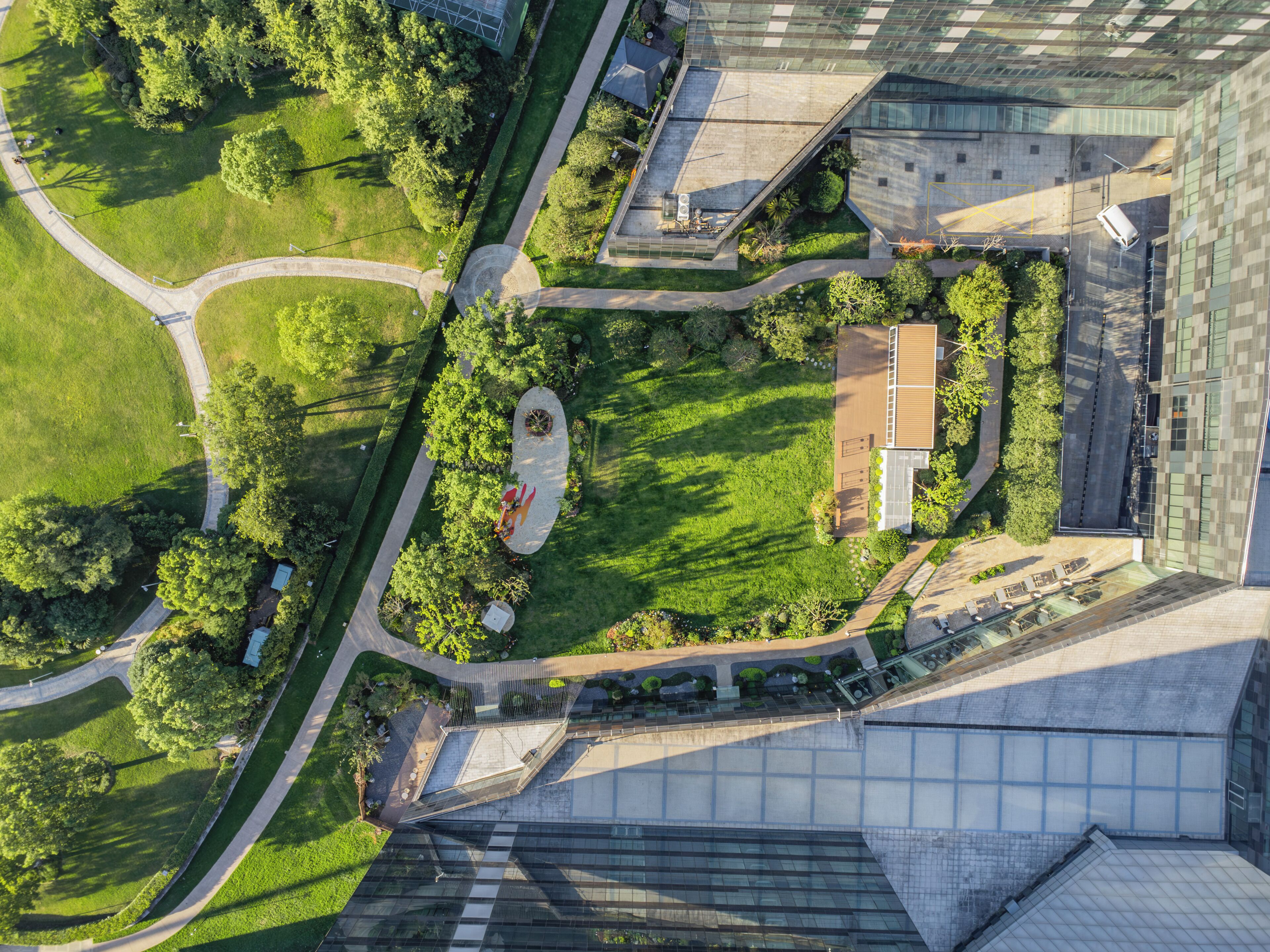 An aerial view of a modern building complex with a central courtyard, surrounding greenery, and a mix of glass and concrete architecture.