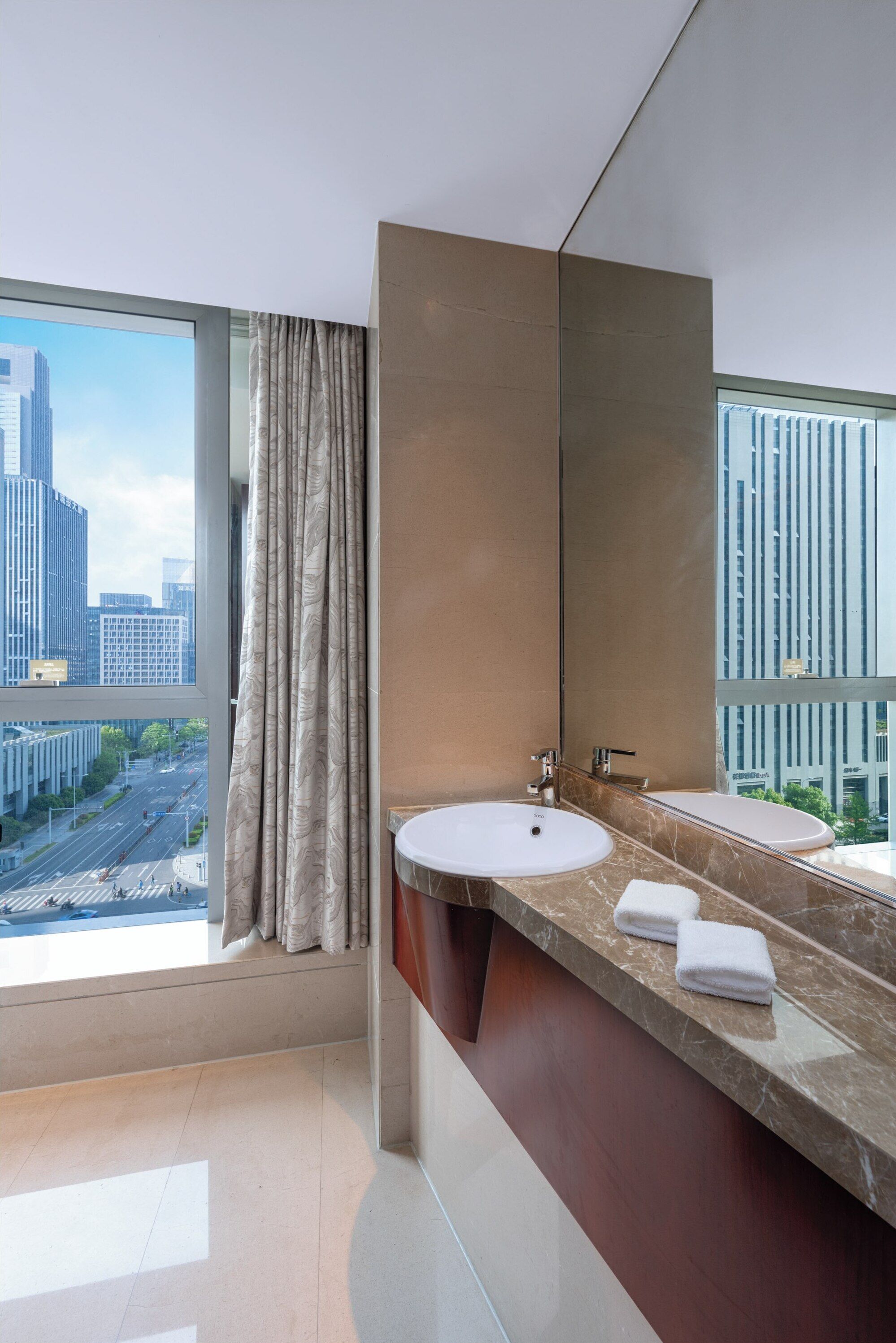 A modern bathroom with a large window, a marble countertop, and a large mirror.