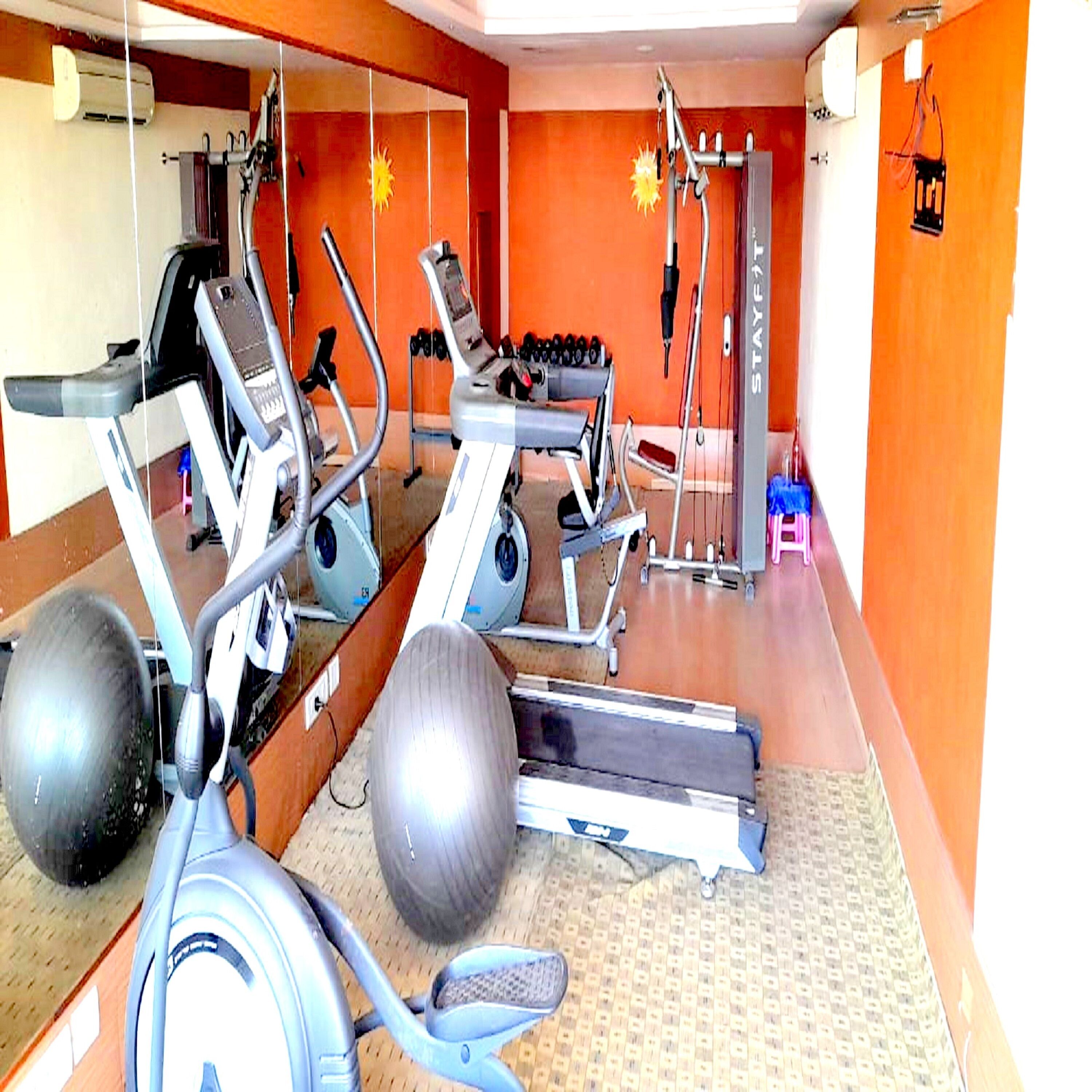 Un gimnasio con equipo de ejercicio, un espejo y un estante fijado a la pared.